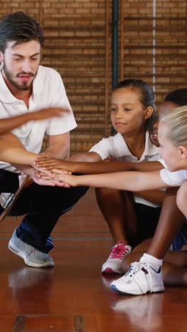 Sports-teacher-and-school-kids-stacking-hands-in-basketball-court