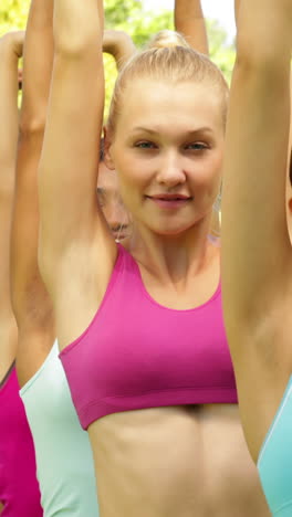 Fitness-class-stretching-their-arms-and-smiling-at-camera-together