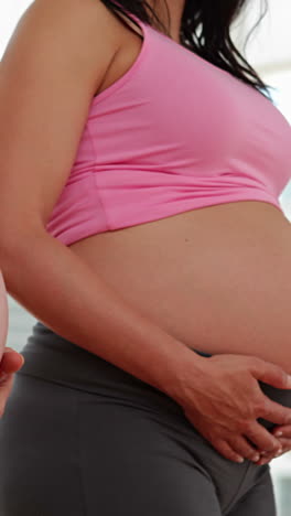 Pregnant-women-standing-in-fitness-studio-holding-their-bumps