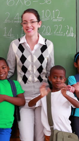 Pupils-and-teacher-waving-and-smiling-at-camera-in-classroom