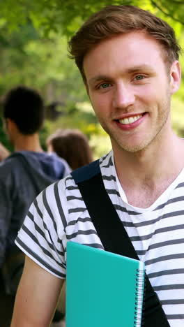 Smiling-student-posing-and-classmates-speaking-behind-him