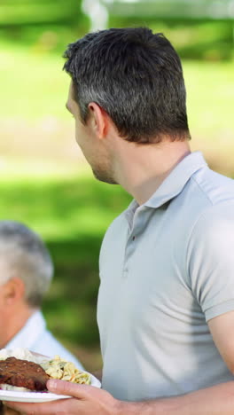 Happy-father-offering-plate-of-food-to-camera-at-family-barbecue