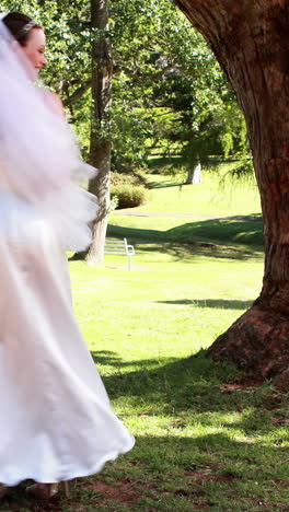 Excited-bride-holding-a-bouquet-in-the-park-smiling-at-camera