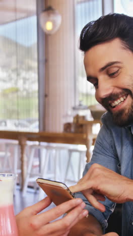 Pareja-Usando-Un-Teléfono-Móvil-Mientras-Toma-Una-Taza-De-Café-Y-Un-Batido