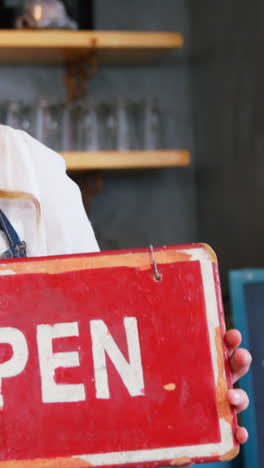 Portrait-of-happy-waitress-is-holding-open-sign