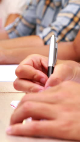 Students-sitting-in-a-line-taking-notes-in-classroom