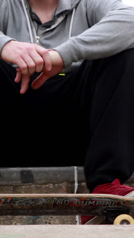 Young-skateboarder-sitting-at-the-outdoor-skatepark