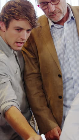 Businessman-and-coworkers-discussing-over-laptop-at-desk