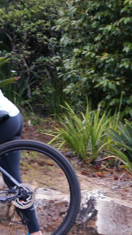 Female-cyclist-walking-with-mountain-bike-in-forest