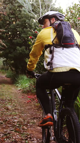 Mountain-biking-couple-riding-in-the-forest-on-a-sunny-day