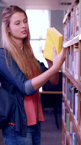 Pretty-blonde-student-taking-book-from-shelf-