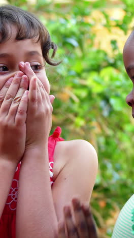 Schoolgirl-whispering-into-her-friend-s-ear-in-campus-at-school