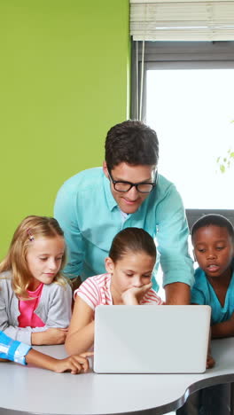 Teacher-and-kids-using-laptop-in-classroom