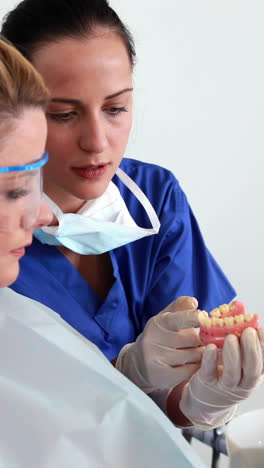 Dentist-speaking-with-patient-showing-model-of-mouth