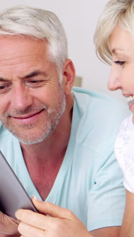 Happy-couple-lying-on-bed-using-tablet-together