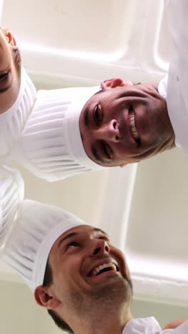 Team-of-chefs-standing-in-circle-looking-down-at-camera