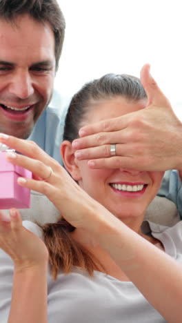 Man-surprising-his-girlfriend-with-a-pink-gift-on-the-sofa