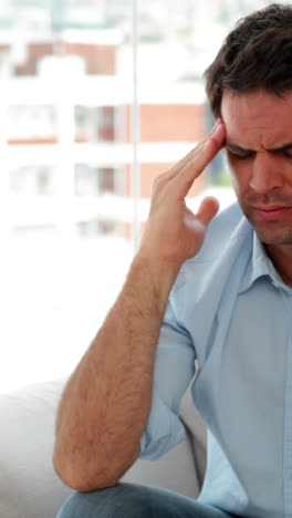 Casual-man-sitting-on-the-sofa-getting-a-headache