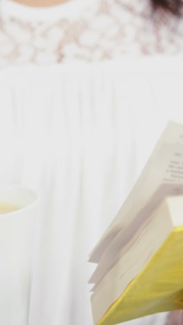 Woman-holding-a-mug-and-a-book-on-sofa-