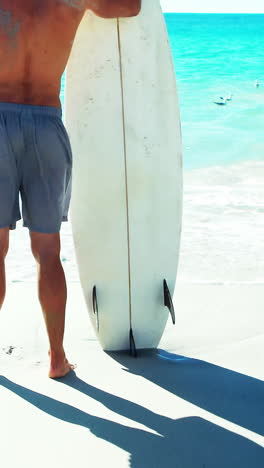 Hombre-De-Pie-En-La-Playa-Con-Tabla-De-Surf