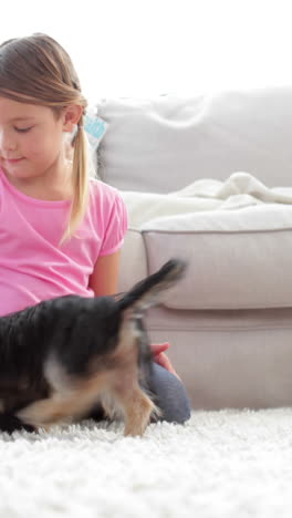 Niña-Jugando-Con-Cachorro-Y-Hueso-Con-Su-Madre-Leyendo-En-El-Sofá.