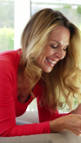 Happy-young-woman-lying-on-bed-and-using-mobile-phone-in-living-room