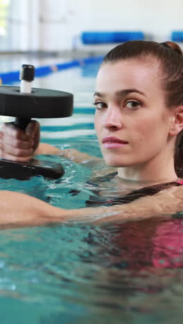 Fit-woman-doing-exercise-with-foam-dumbbells-in-swimming-pool