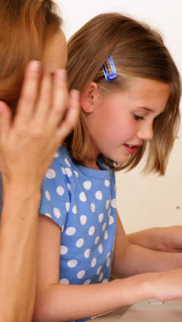 Una-Niña-Usando-Una-Computadora-Portátil-Con-Su-Linda-Madre-En-La-Mesa