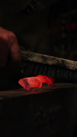 Mid-section-of-blacksmith-using-wire-brush-on-hot-iron