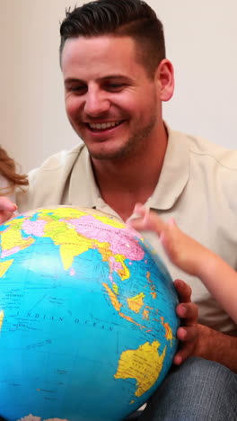 Happy-young-family-sitting-on-sofa-looking-at-globe