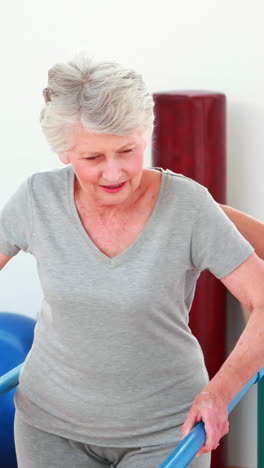 Smiling-physical-therapist-helping-patient-walk-with-parallel-bars