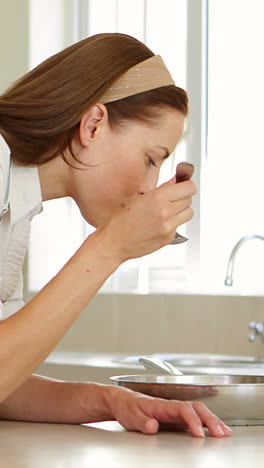 Woman-stirring-and-tasting-something-in-frying-pan-at-the-counter