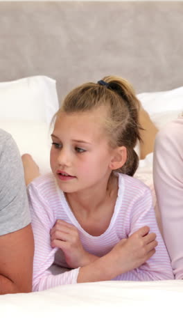 Parents-and-daughter-lying-on-bed-chatting