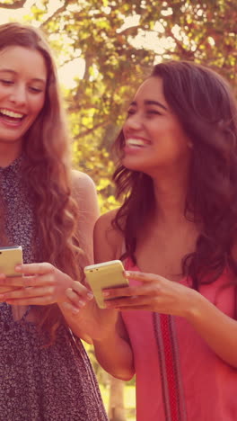 Happy-female-friends-using-their-smartphones-and-laughing