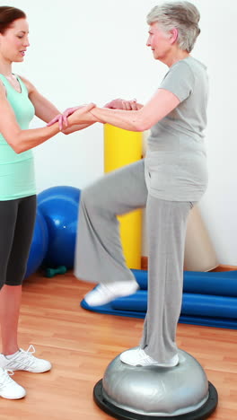 Trainer-helping-elderly-client-to-use-bosu-ball