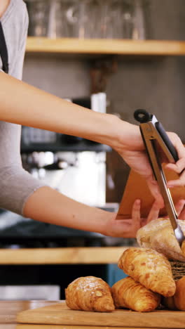 Mid-section-of-waitress-packing-croissants-in-paper-bag