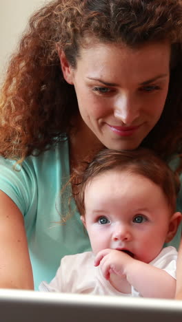 Mother-using-laptop-with-baby-son-on-her-lap