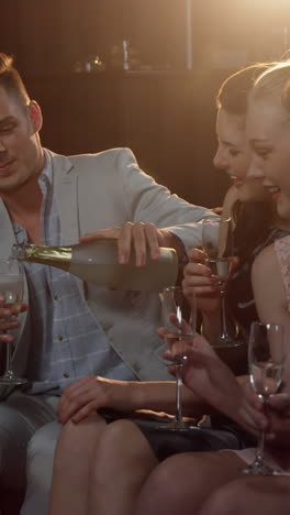 Group-of-smiling-friends-sitting-on-sofa-and-toasting-a-glasses-of-champagne