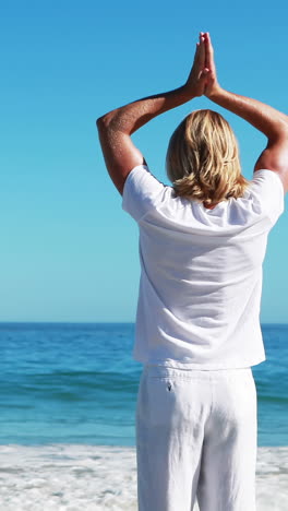 Rear-view-of-man-performing-yoga-at-beach