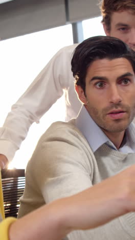 Businessman-and-coworkers-discussing-over-computer-at-desk