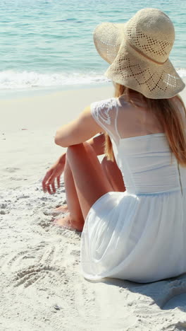 Vista-Trasera-De-Una-Mujer-Rubia-Sentada-En-La-Playa-Y-Mirando-El-Océano