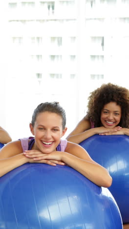 Fitness-class-in-studio-leaning-on-exercise-balls-smiling-at-camera