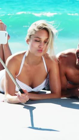 Pareja-Tumbada-En-La-Playa-Y-Tomando-Un-Selfie-Desde-El-Teléfono-Móvil