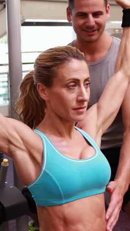 Fit-woman-using-the-weights-machine-for-her-arms-while-trainer-supervises