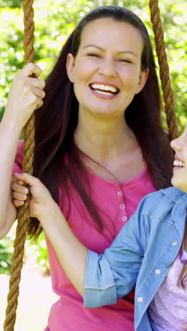 Mother-and-daughter-sitting-on-a-swing-in-the-park-waving-at-camera