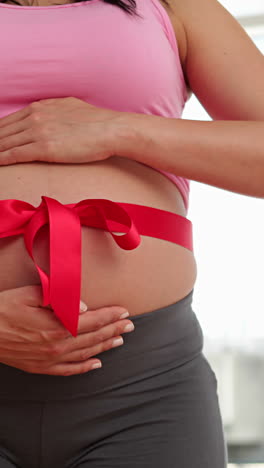 Pregnant-woman-with-a-red-ribbon-around-her-bump-smiling-at-camera