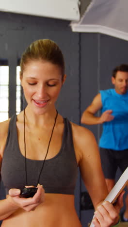 Female-trainer-looking-at-stop-watch-while-people-exercising