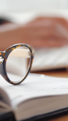 Close-up-of-personal-organizer-and-spectacle-while-businesswoman-working-over-computer