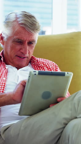 Mature-man-sitting-on-sofa-and-using-digital-tablet-in-living-room