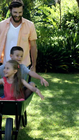 Glückliche-Familie-Spielt-Mit-Der-Schubkarre-Im-Garten